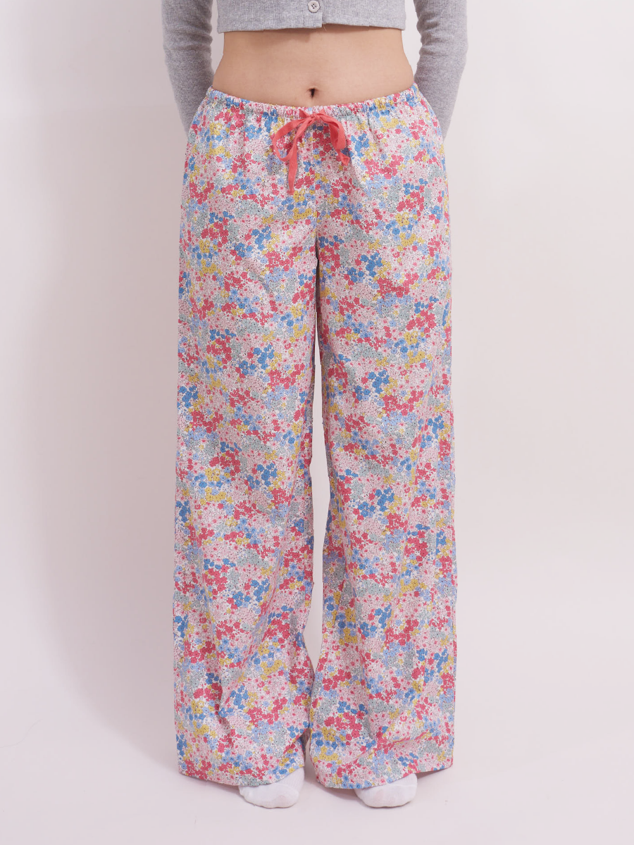 Front view of low-rise wide leg lounge pants in pastel pink ditsy floral print with a red drawstring. Crafted from 100% cotton, these pants are perfect for summer lounging or as cozy pyjamas.