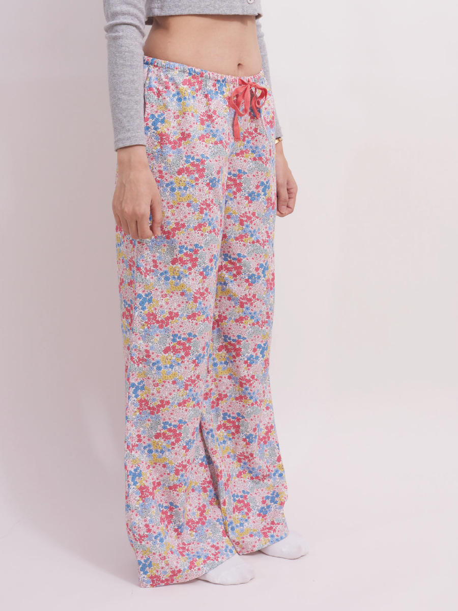 Side view of low-rise wide leg lounge pants in pastel pink ditsy floral print. These 100% cotton pants are designed for a relaxed fit with a red drawstring at the waist, ideal for casual lounging or sleep.