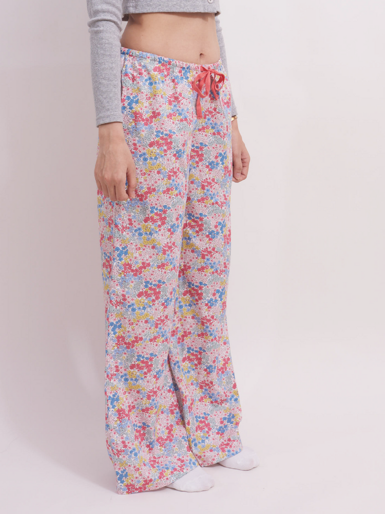 
                                            
                                                Side view of low-rise wide leg lounge pants in pastel pink ditsy floral print. These 100% cotton pants are designed for a relaxed fit with a red drawstring at the waist, ideal for casual lounging or sleep.
                                            
                                        