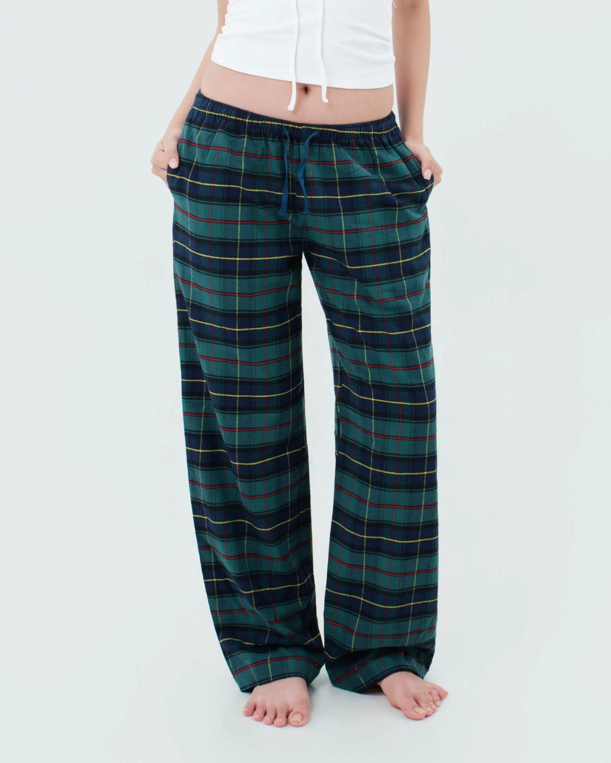 A woman wearing loose, low-rise wide-leg plaid pajama pants in dark green and navy with thin yellow, red and white stripes